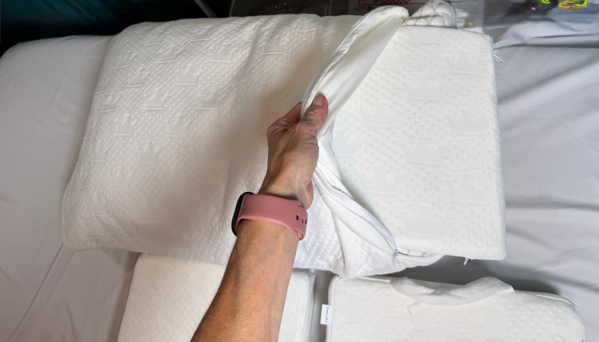A hand lifting the zippered flap of the Crown Lift pocket pillowcase to slide a support core inside.